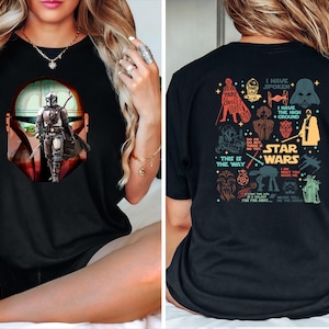 May include: Black t-shirt featuring a graphic of The Mandalorian with a Baby Yoda. The front design shows the character in a helmet and armor. The back of the shirt has various Star Wars character illustrations and text, including "Star Wars" and "This is the Way."