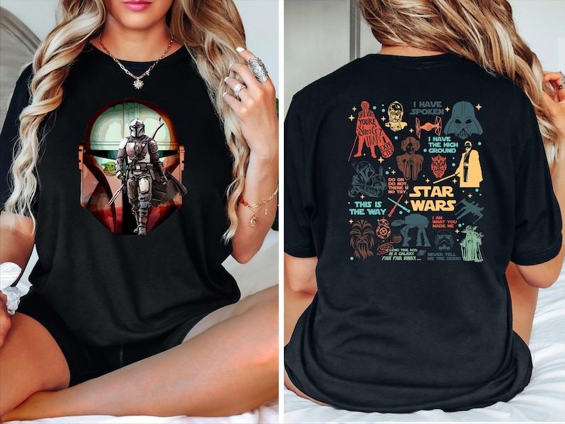 May include: Black t-shirt featuring a graphic of The Mandalorian with a Baby Yoda. The front design shows the character in a helmet and armor. The back of the shirt has various Star Wars character illustrations and text, including "Star Wars" and "This is the Way."