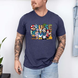 May include: Navy blue V-neck t-shirt featuring the word "CRUISE" in colorful letters, with cartoon characters. The characters include Mickey Mouse, Minnie Mouse, Donald Duck, and Goofy. The shirt is made of a soft material.