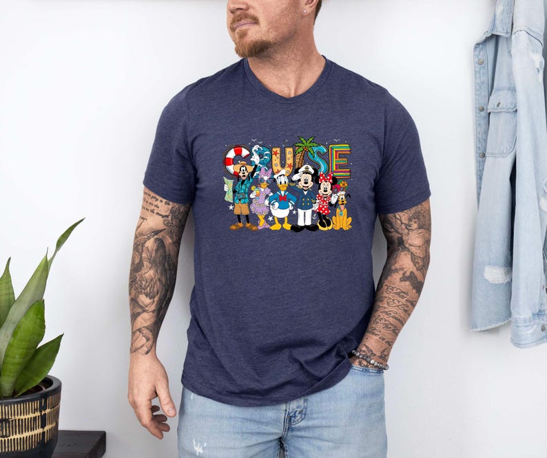 May include: Navy blue V-neck t-shirt featuring the word "CRUISE" in colorful letters, with cartoon characters. The characters include Mickey Mouse, Minnie Mouse, Donald Duck, and Goofy. The shirt is made of a soft material.