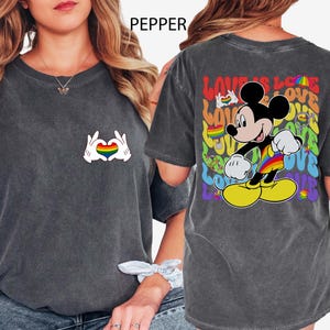 May include: Dark gray t-shirt featuring a rainbow heart design made by hands on the front. The back of the shirt has a colorful Mickey Mouse graphic with the words "LOVE IS LOVE".