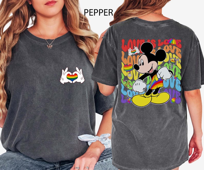 May include: Dark gray t-shirt featuring a rainbow heart design made by hands on the front. The back of the shirt has a colorful Mickey Mouse graphic with the words "LOVE IS LOVE".