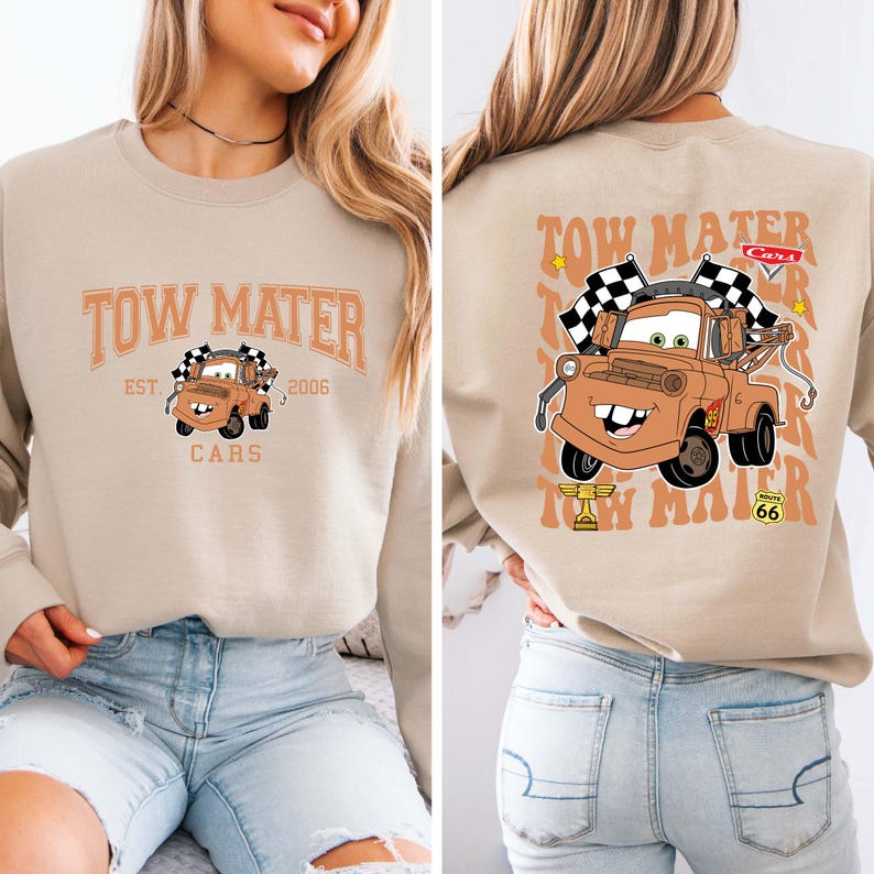 Peut inclure: Sweat-shirt beige avec une image de dessin anim&eacute; de Martin la d&eacute;panneuse du film Cars. Le devant affiche "Tow Mater" au-dessus de l'image, avec "EST. 2006" et "CARS" en dessous. Le dos pr&eacute;sente une image plus grande de Martin avec des drapeaux &agrave; damiers.
