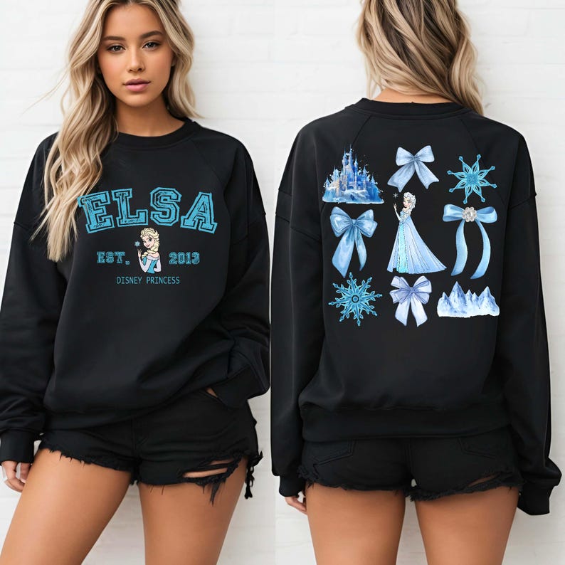 以下が含まれることがあります： 青い文字で「ELSA」と書かれた黒いスウェットシャツ。下に「EST. 2013」と「DISNEY PRINCESS」と書かれています。スウェットシャツの背面には、エルサ、リボン、雪の結晶、お城が青色で描かれています。