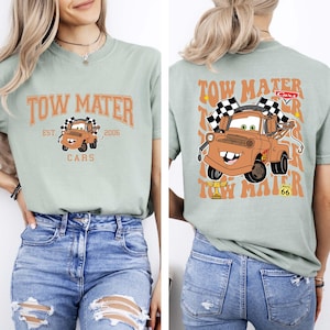 Puede incluir: Camiseta verde claro con una imagen de dibujos animados de Mate de la pel&iacute;cula Cars. La parte delantera de la camiseta tiene el texto "Tow Mater" y "Cars". La parte trasera tiene una imagen m&aacute;s grande de Mate con banderas a cuadros.