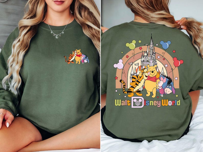 Op de afbeelding: Olijfgroene sweatshirt met een cartoonontwerp van Winnie de Poeh, Teigetje en Iejoor. De voorkant heeft een kleine afbeelding van de personages. De achterkant toont een regenboog, kasteel en de tekst "Walt Disney World."