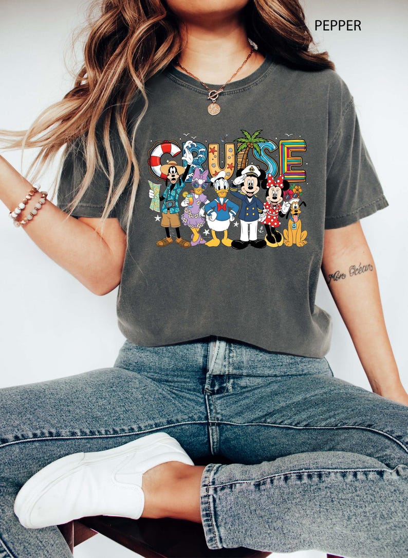 May include: Dark gray t-shirt with a colorful "CRUISE" graphic featuring Disney characters. The design includes Mickey Mouse, Minnie Mouse, Donald Duck, Goofy, and Pluto, with nautical elements like a life preserver and palm trees.
