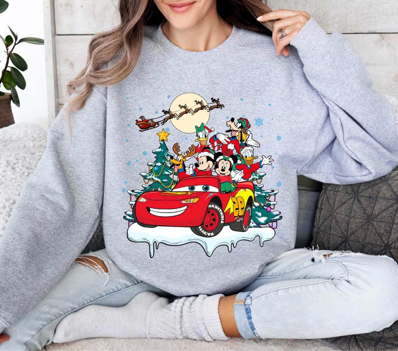 K&ouml;nnte beinhalten: Ein hellgraues Sweatshirt mit einem weihnachtlichen Design. Die Grafik zeigt ein rotes Rennauto mit Mickey und Minnie Mouse, Donald Duck und Goofy. Ein Weihnachtsbaum, Schneeflocken und der Schlitten des Weihnachtsmanns vervollst&auml;ndigen die Szene.
