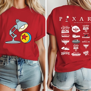 May include: Red t-shirt featuring a cartoon image of the Pixar lamp and ball on the front. The back of the shirt displays the Pixar logo and logos from various Pixar movies, including Toy Story, Cars, and Finding Nemo.