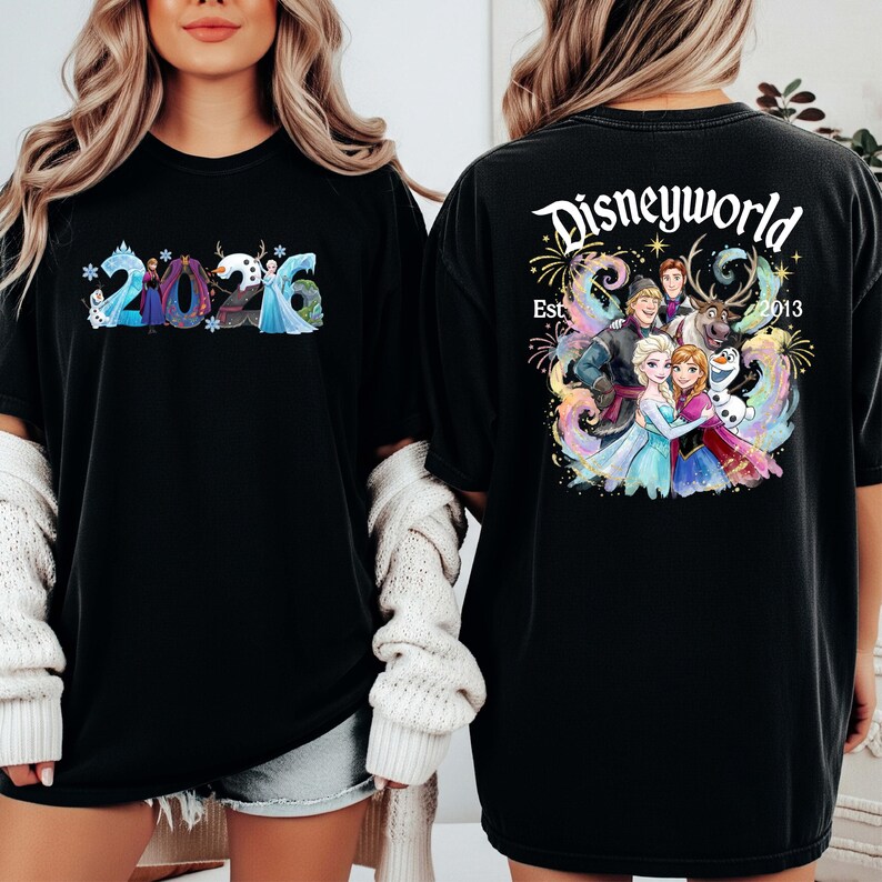 K&ouml;nnte beinhalten: Schwarzes T-Shirt mit dem Text "2026" in einem Schneeflocken-Design auf der Vorderseite. Auf der R&uuml;ckseite des Shirts steht "Disneyworld Est. 2013" mit einer farbenfrohen Grafik von Figuren aus dem Film Frozen.