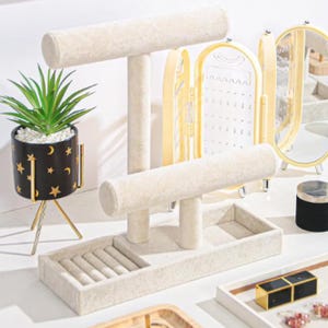 May include: A jewellery organiser set featuring a beige velvet bracelet stand, a yellow jewellery case, and a small black pot with a gold stand. The pot is decorated with gold stars and crescent moons. The set is designed for organising jewellery.