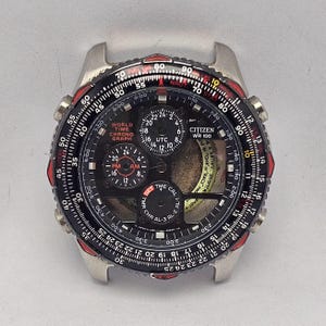 Könnte beinhalten: Ein Citizen World Time Chronograph Zifferblatt mit schwarzem Zifferblatt, mit mehreren Hilfszifferblättern und roten Akzenten. Das Zifferblatt zeigt verschiedene Zeitzonen und Funktionen, einschließlich UTC und Chronograph.