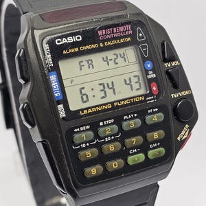 May include: A black Casio Wrist Remote Controller watch featuring a digital display showing FR 4-24 and 6:34.43. The watch includes an integrated keypad with numbered buttons, playback controls, and labels for TV volume, channel, and power functions.