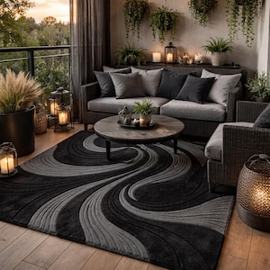 May include: An outdoor seating area with a grey sofa, dark cushions, and a circular coffee table. A black and grey patterned rug covers the floor. Hanging plants and fairy lights create a relaxing atmosphere. Lanterns with candles provide soft lighting.
