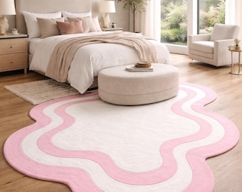 May include: A bedroom scene featuring a large, wavy-edged rug with a pink and white design. The rug is on a hardwood floor, and the room includes a bed, ottoman, and armchair, creating a cozy atmosphere.