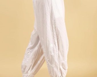 Può includere: Pantaloni bianchi in cotone con dettagli floreali ricamati e rifiniture in pizzo alle caviglie. I pantaloni hanno una vestibilità ampia e sono abbinati a sandali bianchi. La vita con coulisse aggiunge comfort.