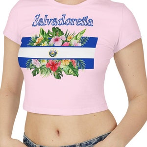 Peut inclure: Un t-shirt rose court avec un motif floral représentant le drapeau du Salvador et le texte "Salvadoreña".