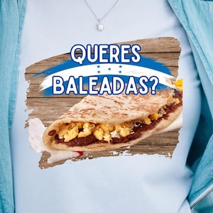 May include: A white t-shirt with a graphic of a Honduran baleada, a traditional dish, on a wooden background. The text "Quieres Baleadas?" is written in blue above the baleada.
