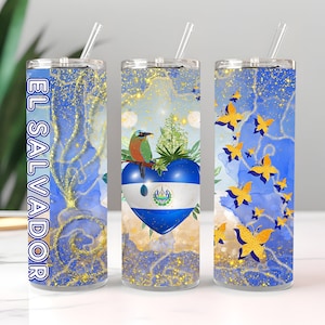 May include: Three stainless steel tumblers with a blue and gold glitter background. The center tumbler features a heart with the El Salvador flag and a bird perched on a branch. The other two tumblers have a design of gold butterflies on a blue background. The text "EL SALVADOR" is printed on the left tumbler.