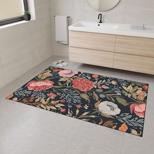 May include: A rectangular floral bath mat with a dark navy background, adorned with large, colourful flowers in pink, coral, and white. Green and yellow foliage complements the design. The mat is in a bathroom setting.