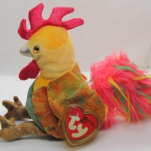 Puede incluir: Un juguete de peluche de gallo con cabeza amarilla, cresta y barbilla rojas y cola colorida. El gallo tiene una etiqueta TY Zodiac adjunta. El cuerpo es una mezcla de naranja, verde y amarillo. La cola es rosa con detalles amarillos y verdes.