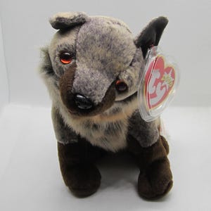 May include: A plush toy wolf with brown and gray fur, red eyes, and a black nose. The wolf has a tag attached to its ear. The toy is sitting upright.