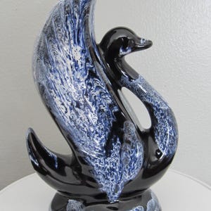 May include: A ceramic swan ornament with a glossy black body and a wing with a blue and white marbled design. The swan sits on a round base, a decorative accent piece for the home.