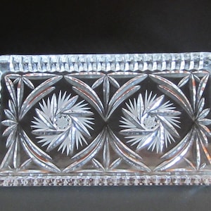 Może przedstawiać: Prostokątny, przezroczysty szklany talerz z misternymi, wytrawionymi wzorami rozgwieżdżonych gwiazd i liści. Krawędzie talerza mają teksturowany, powtarzalny wzór. Talerz jest prawdopodobnie przeznaczony do serwowania lub ekspozycji.