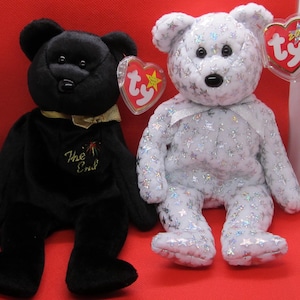 Könnte beinhalten: Zwei Plüschteddys. Einer ist schwarz mit einer goldenen Schleife und dem Text "The End". Der andere ist weiß mit silbernen Sternen. Beide haben Ty-Herzanhänger.