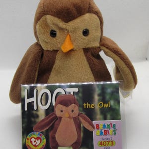 Peut inclure: Une peluche en forme de hibou brun avec un bec orange et des yeux noirs. Le hibou est un Beanie Baby, avec une étiquette indiquant "HOOT the Owl" et "Beanie Babies Series I 4073 1998". L'objet est de collection.