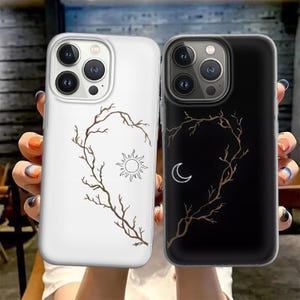 以下が含まれることがあります： 白と黒の2つの携帯電話ケース。それぞれ自然をモチーフにしたデザインです。白いケースには太陽と枝のデザインがあります。黒いケースには月と枝のデザインがあります。