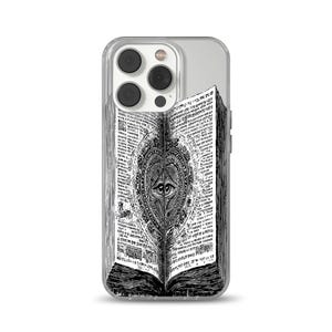 Peut inclure: Coque de téléphone transparente avec une illustration en noir et blanc d'un livre ouvert. Les pages du livre sont remplies de texte et d'un motif central d'un œil dans un cadre en forme de cœur. La coque a un dos transparent et un module caméra argenté.