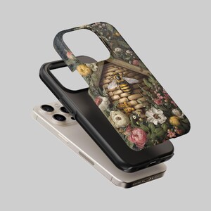 May include: A phone case featuring a detailed illustration of a bee and a beehive surrounded by colorful flowers. The case has a black border and is layered over a silver phone.