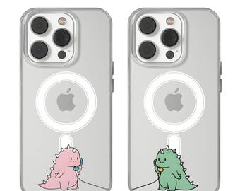 May include: Two clear phone cases with a cartoon dinosaur design. One case features a pink dinosaur, the other a green dinosaur, both holding a telephone. The cases have a white circular design and an Apple logo.