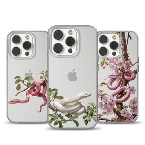 Può includere: Tre custodie trasparenti per telefono con illustrazioni di serpenti. Una custodia presenta un serpente rosa su un ramo, un'altra un serpente bianco e la terza un serpente rosa tra fiori rosa. Le custodie hanno un design trasparente.