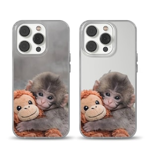 Op de afbeelding: Transparante telefoonhoesjes met een grijze aap die een oranje pluche aap knuffelt. De telefoonhoesjes hebben een transparante rand en een grijze achtergrond. De afbeelding is een close-up van de apen.