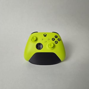 Könnte beinhalten: Ein limettengrüner kabelloser Videospiel-Controller mit einem schwarzen Steuerkreuz, zwei Analogsticks und vier Aktionstasten mit der Beschriftung Y, X, B und A. Der Controller verfügt über eine zentrale Xbox-Logo-Taste und einen schwarzen Griffbereich.