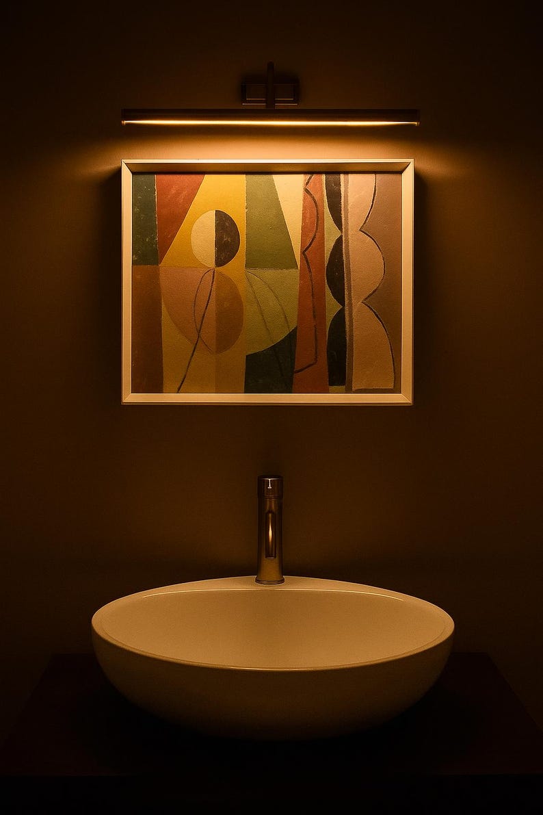 May include: A white oval vessel sink with a tall metallic faucet positioned below a rectangular framed painting. The artwork features abstract geometric shapes in shades of yellow, green, red, and black, illuminated by a horizontal wall light.