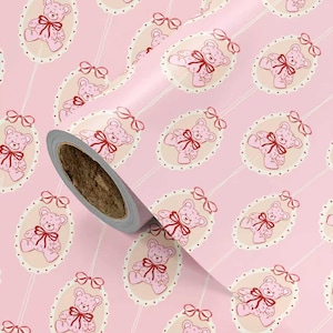 Pode incluir: Papel de embrulho rosa com um padr&atilde;o repetido de ursinhos de pel&uacute;cia rosa com la&ccedil;os vermelhos dentro de molduras ovais. O papel est&aacute; em um rolo. O fundo &eacute; rosa claro. O n&uacute;cleo do rolo &eacute; marrom.