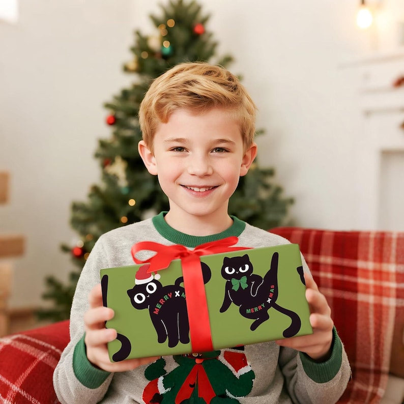 May include: A wrapped gift with a green background and black cat illustrations wearing a Santa hat and bow tie. The gift is tied with a red ribbon and bow. The words "Merry Xmas" are printed on the gift. A young person is holding the gift.