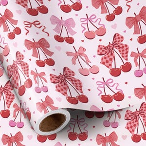 May include: A roll of patterned paper featuring a repeating design of cherries and bows in shades of red and pink. The bows have solid and checkered patterns, with small pink hearts scattered across the white background.