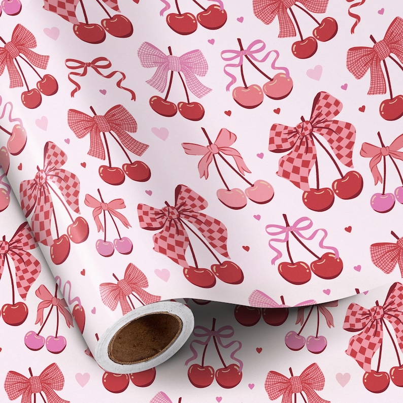 May include: A roll of patterned paper featuring a repeating design of cherries and bows in shades of red and pink. The bows have solid and checkered patterns, with small pink hearts scattered across the white background.