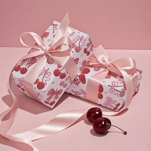 May include: Two wrapped gifts with pink satin bows and cherry-patterned paper. The gifts are on a pink surface, with two cherries and a length of pink ribbon. The wrapping paper features red cherries, bows, and hearts.