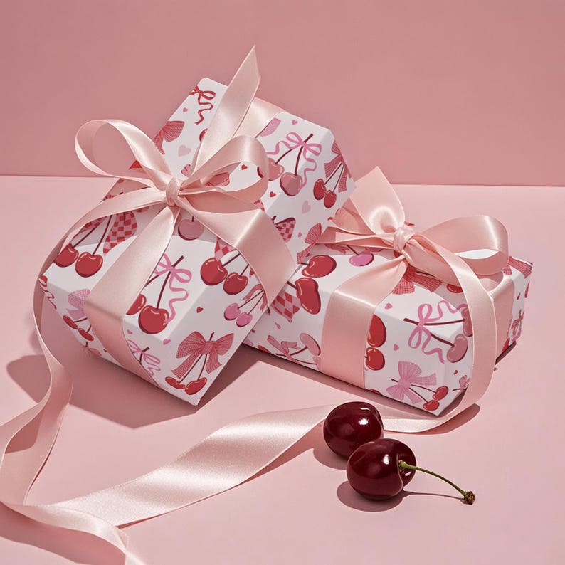 May include: Two wrapped gifts with pink satin bows and cherry-patterned paper. The gifts are on a pink surface, with two cherries and a length of pink ribbon. The wrapping paper features red cherries, bows, and hearts.