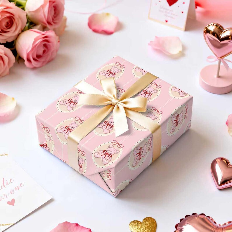 Pode incluir: Uma caixa de presente rosa com um padr&atilde;o de ursinhos, amarrada com uma fita dourada. Rodeada por rosas cor-de-rosa, p&eacute;talas e decora&ccedil;&otilde;es em forma de cora&ccedil;&atilde;o, criando um ambiente rom&acirc;ntico e festivo.