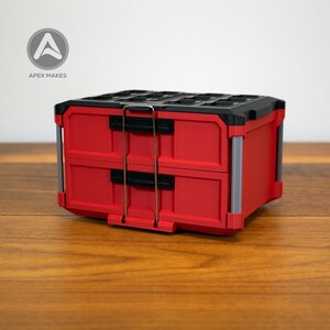 Puede incluir: Un contenedor de almacenamiento rojo y negro de dos cajones con detalles plateados. El contenedor tiene una parte superior negra y asas plateadas. El logotipo "Apex Makes" está en la esquina superior izquierda. El contenedor está sobre una superficie de madera.