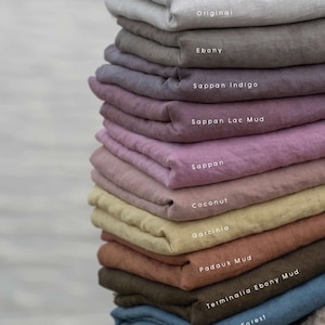 May include: A vertical stack of folded fabric pieces in various colors, each labeled with text: Original, Ebony, Sappan Indigo, Sappan Lac Mud, Sappan, Coconut, Garcinia, Padauk Mud, Terminalia Ebony Mud, and Indigo Forest. The textiles have a matte finish.