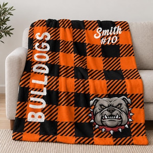 Könnte beinhalten: Eine schwarz-orange karierte Decke mit dem vertikal in Weiß gedruckten Wort BULLDOGS, dem Text Smith #10 in Weiß und einer grafischen Darstellung einer knurrenden Bulldogge mit rotem Stachelhalsband in der Ecke.
