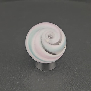 May include: A spherical glass marble featuring a swirling pattern of pastel pink, light blue, and white colors. The surface of the marble is smooth and glossy, with the spiral design converging toward a central point on the top of the sphere.