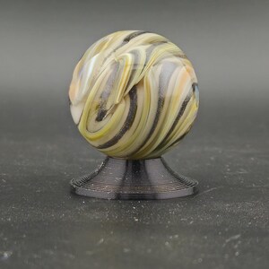 May include: A decorative glass marble with swirling patterns of yellow, black, and white, on a black, spiral-shaped stand. The marble's design resembles natural stone. The stand is approximately 2.5 cm in diameter.